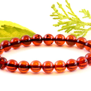 A bracelet made of perfect round red amber beads with a white background and a green leaf in the background.