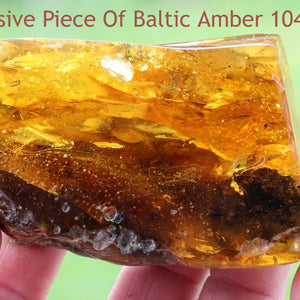 A hand holding a polished piece of Baltic amber with natural color variations and inclusions.