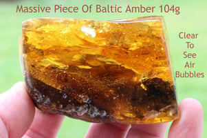 A hand holding a polished piece of Baltic amber with natural color variations and inclusions.