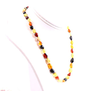 A necklace with flat, round amber beads in various shades of yellow, honey, cognac, and white strung together, displayed on a mannequin.